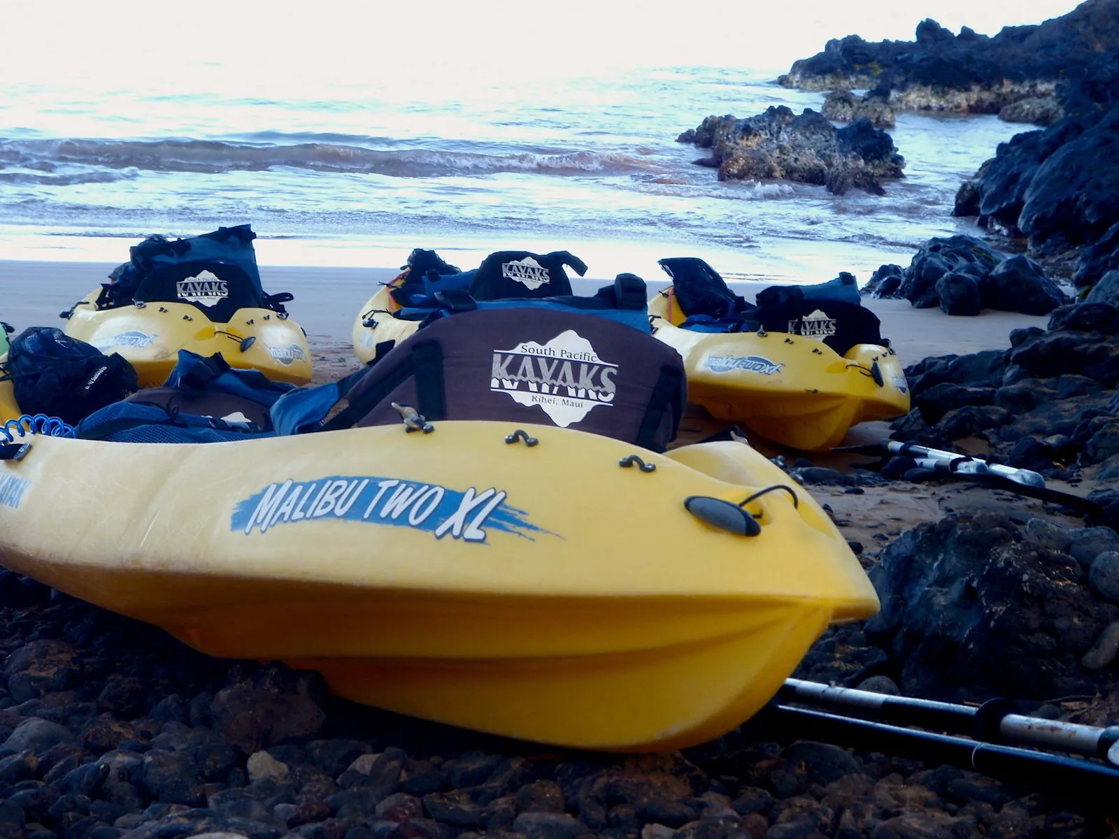 South Pacific Kayaks tandem kayaks lined up on a beach by black lava rocks