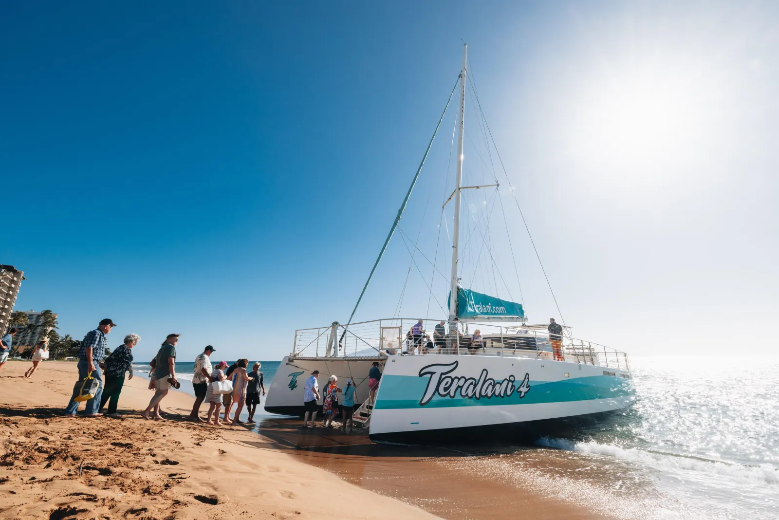 Guests lining up on the sand to board the Teralani 4 catamaran