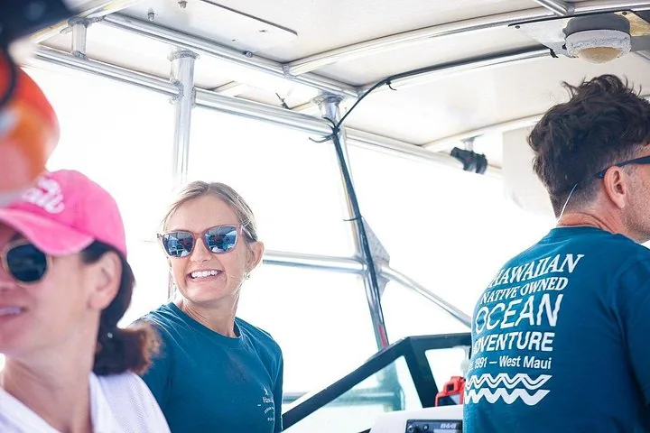 Smiling crew member in sunglasses under the raft canopy beside guests