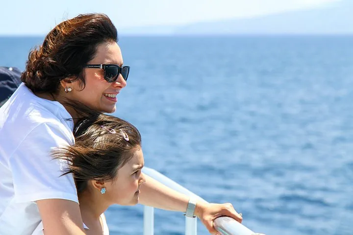 Woman and young girl leaning on a boat rail, looking out over the blue sea