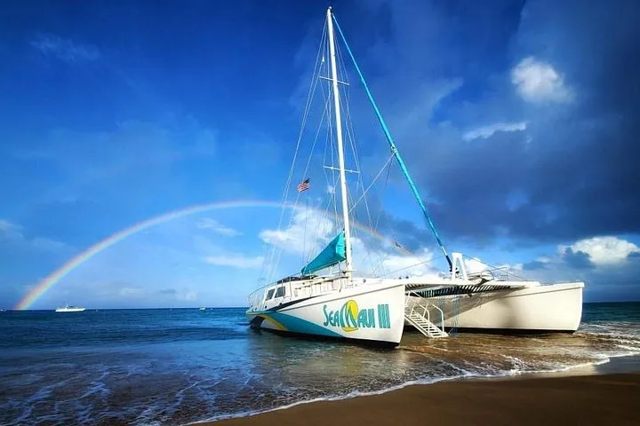Sea Maui III catamaran pulled up on the sand with boarding stairs and a rainbow