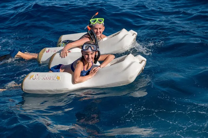 Two smiling children in masks and snorkels riding white sea boards