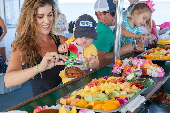 Woman and toddler serving themselves fruit and muffins from a buffet on board