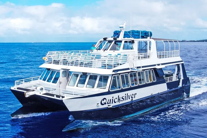 White double-deck Quicksilver catamaran cruising across deep blue water under scattered clouds