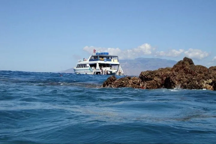 White catamaran anchored beyond a dark rocky outcrop with a hazy island behind