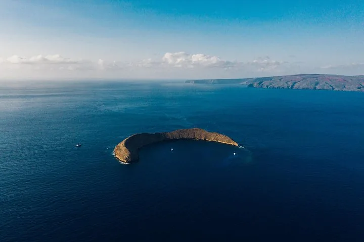 Aerial view of crescent-shaped Molokini islet in deep blue sea with boats moored inside