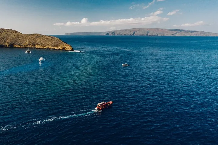 Red raft speeding toward a crescent islet where small boats are moored