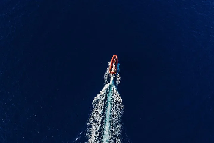 Overhead view of a red raft leaving a long white wake across open ocean