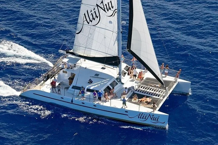 Aerial view of the Alii Nui catamaran under white sails with guests relaxing on deck