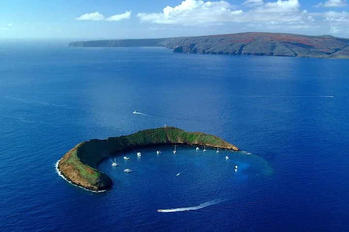 Aerial view of crescent Molokini with boats moored in its cove and an island behind