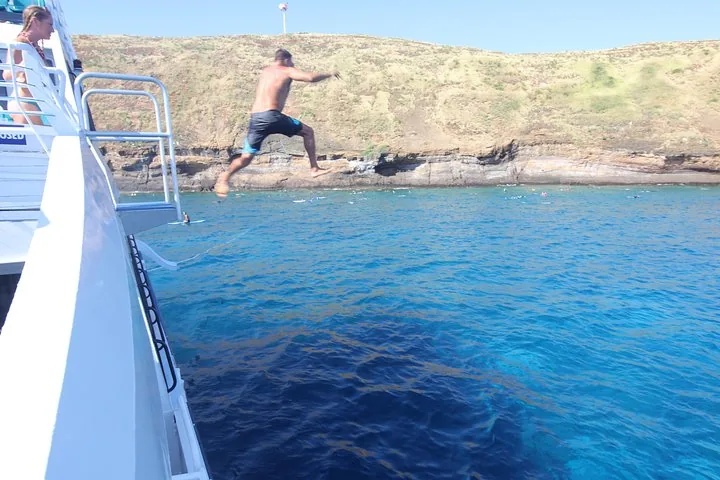 Man leaping off the side of a white catamaran into clear blue water
