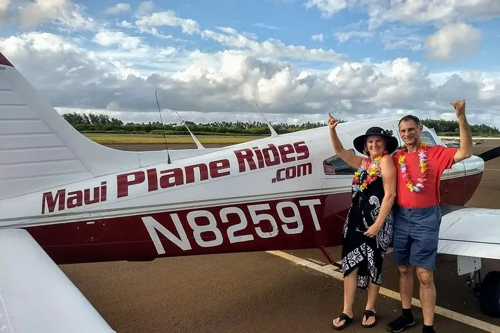 Smiling couple in flower lei beside a white and maroon Maui Plane Rides airplane