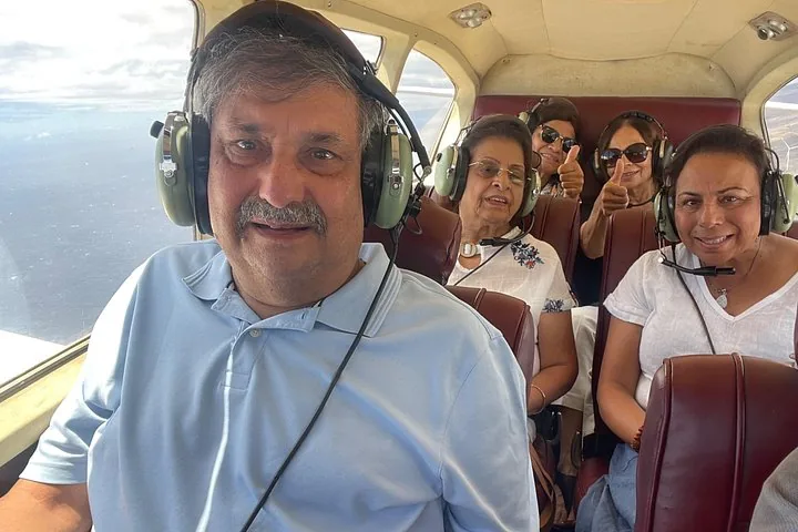 Five smiling passengers wearing headsets seated in a small airplane cabin over the ocean