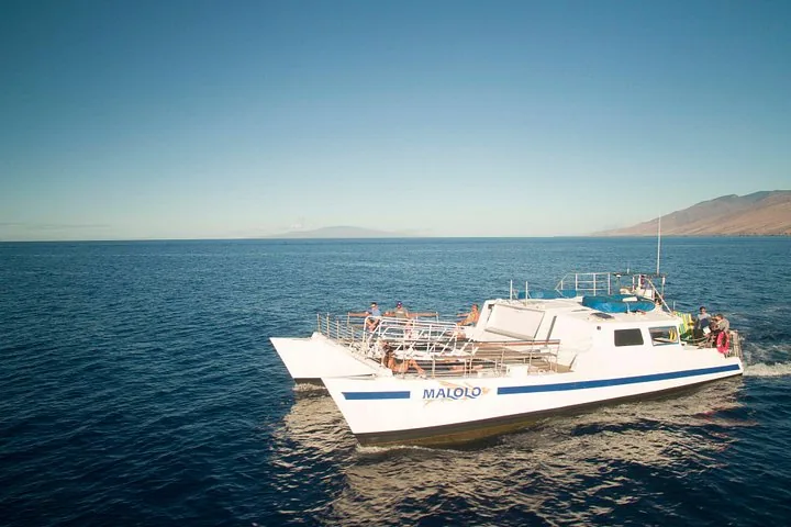 The Malolo catamaran under way with guests on the front deck, island on the horizon